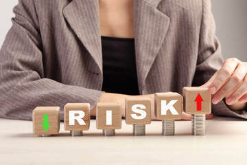 Business risk. Woman putting wooden cube with arrow onto stacked coins at table. closeup