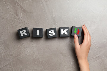 Woman putting cube with arrows next to word Risk on grey table, top view