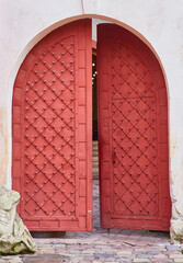 Ancient red arched gate with metal studs in a historic stone wall.