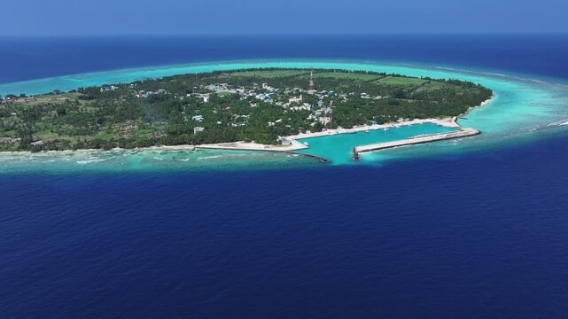 Aerial view of Thoddoo, where turquoise waters meet lush greenery, fringed by a vibrant coral reef and a protective port, Thoddoo, Alif Alif Atoll, Maldives.