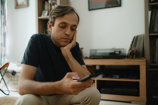 Sad man with mobile phone sitting at home