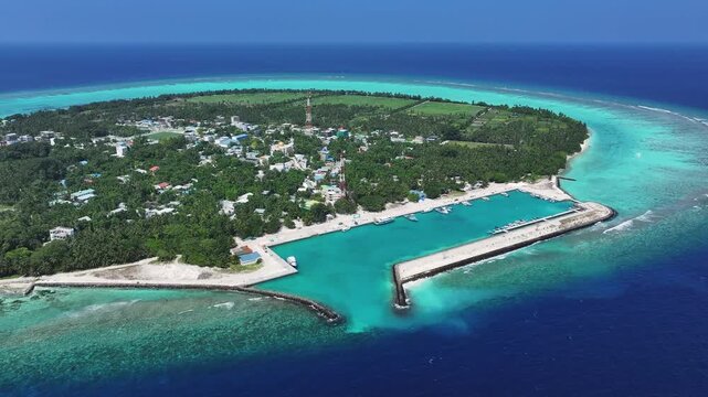 Aerial view of Thoddoo Island, a lush green island with a vibrant marina contrasting against the deep blue ocean, Thoddoo, Alif Alif Atoll, Maldives.