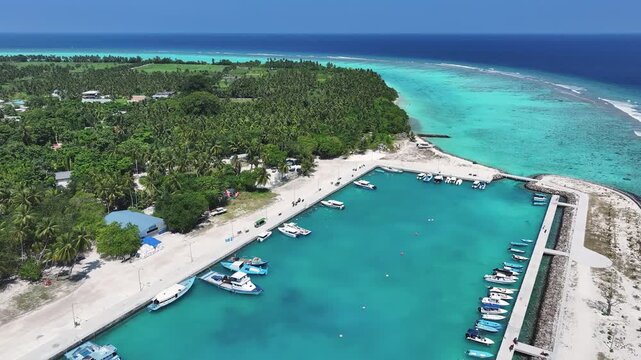 Aerial view of boats docked at the Thoddoo pier, contrasting turquoise waters with the lush greenery of the island, Thoddoo, Alif Alif Atoll, Maldives.