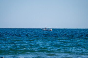 A solitary boat floats peacefully on the deep blue sea beneath a cloudless sky, surrounded by tranquil waves.