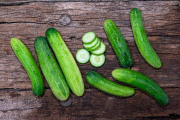 cucumber (Cucumis sativus) and slices on wood background. Freshly sliced mini cucumbers with knife on wooden cutting board.