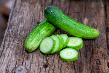 cucumber (Cucumis sativus) and slices on wood background. Freshly sliced mini cucumbers with knife on wooden cutting board.