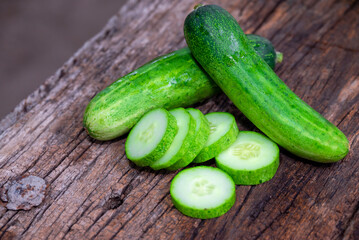 cucumber (Cucumis sativus) and slices on wood background. Freshly sliced mini cucumbers with knife on wooden cutting board.