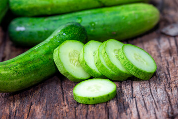 cucumber (Cucumis sativus) and slices on wood background. Freshly sliced mini cucumbers with knife on wooden cutting board.