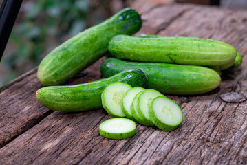 cucumber (Cucumis sativus) and slices on wood background. Freshly sliced mini cucumbers with knife on wooden cutting board.