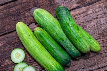 cucumber (Cucumis sativus) and slices on wood background. Freshly sliced mini cucumbers with knife on wooden cutting board.