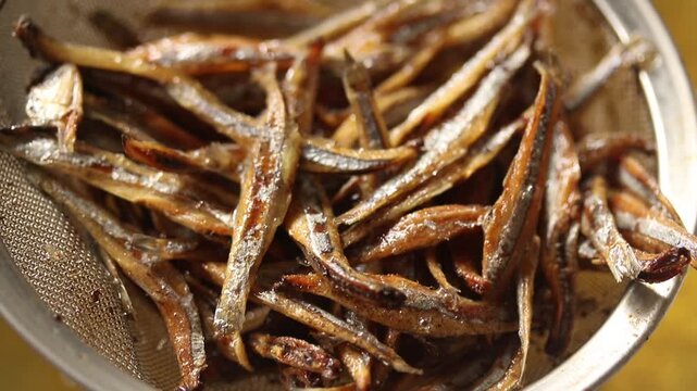 Lift the stainless steel strainer containing the fried small dried anchovies fish out of the boiling oil.