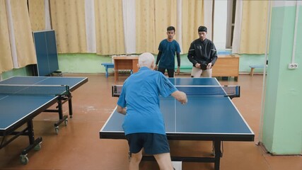 Two young athletes face senior opponent in intense indoor table tennis match, showing competition, discipline, teamwork, focus, speed, and generational sportsmanship during training session - Powered by Adobe