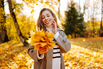 A happy woman is having fun in an autumn park at sunset. A beautiful woman in casual clothes throws leaves into the air on a sunny day. Concept of a walk, relaxation.