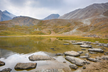Idyllic summer landscape with hiking trail in the mountains with beautiful fresh green mountain pastures, lake with reflection. Kyrgyzstan