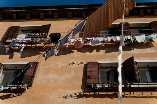 Sunlit wall of a Venetian building with drying clothes and textiles hanging from lines, a glimpse into daily traditions and timeless atmosphere of authentic Venice neighborhoods - Powered by Adobe
