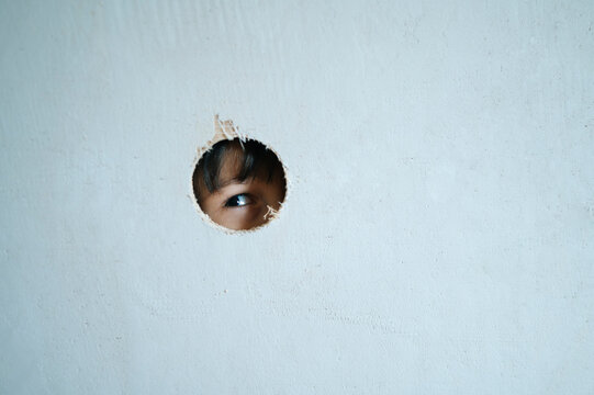 Child peeking through a hole in a wall during house renovation