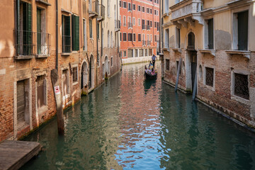Narrow waterway in Venice lined with old buildings and a gondolier guiding passengers through the lagoon city