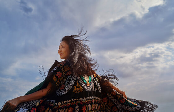 Smiling woman dancing outdoors in colorful chapan under dramatic sky