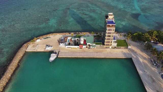Aerial view of modern building with boat, turquoise water, and palm trees, creating a vibrant contrast of colors and textures, Kamadhoo, Baa Atoll, Maldives.