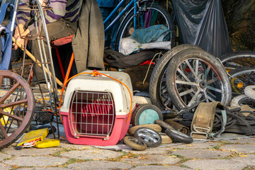 Flea market of antiques with pink pet carrier, old wheels, bicycle parts, and used items displayed for sale.