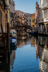 Venetian canal with wooden pedestrian bridge, moored boats and colorful historic facades reflecting in calm water, capturing authentic Italian architecture and urban waterway design