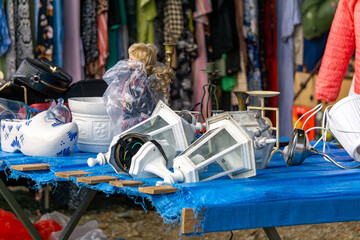 Flea market stall with porcelain, garden lamps, doll in plastic wrap, and second-hand clothes...
