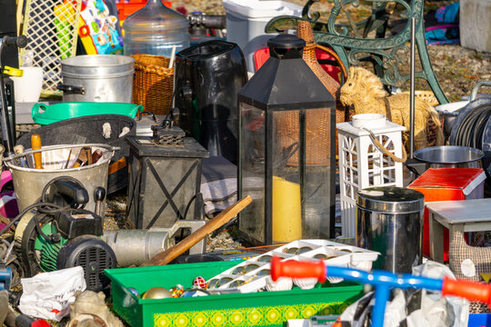 Flea market with assorted items: lanterns, buckets, baskets, toys and garden equipment displayed chaotically on vendor stall.