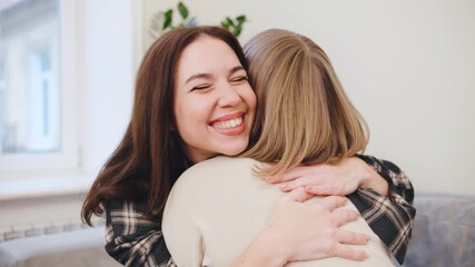 Adult daughter shares a joyful moment while hugging her elderly mother at home on a warm afternoon