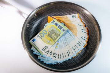 Stacks of euro banknotes placed inside a frying pan, symbolizing money, finance, savings,...