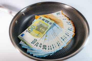 Stacks of euro banknotes placed inside a frying pan, symbolizing money, finance, savings,...