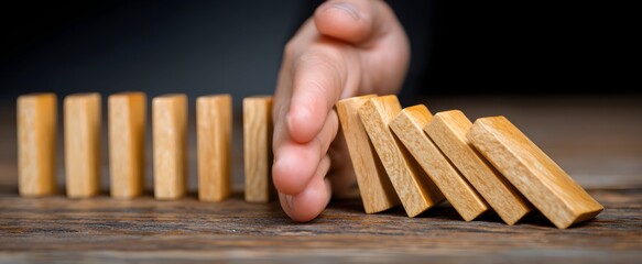 The hand halts falling wooden dominoes avoiding a destructive chain reaction.