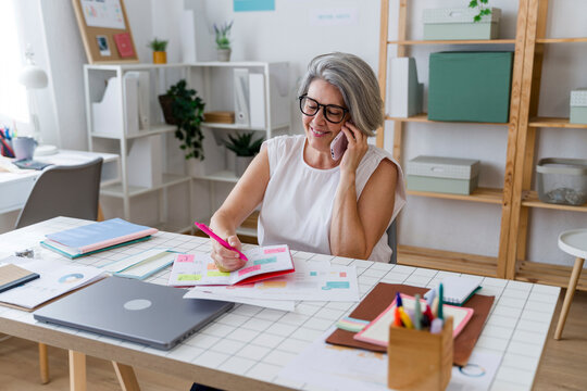 Businesswoman multitasking at office desk with smartphone and planner