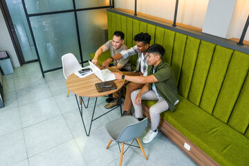 Asian Men Collaborating on Business Looking at Laptop and Pointing to Screen in Modern Office Space