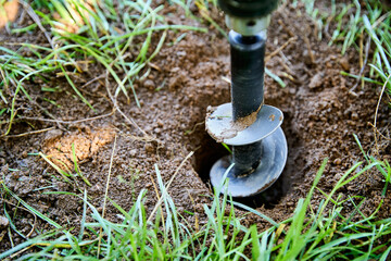 Garden auger drill bit digging hole in soil for planting and construction work