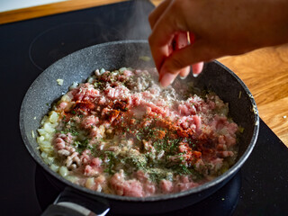 Frying bolognese sauce - seasoning dish with minced pork meat in frying pan, close-up of hand