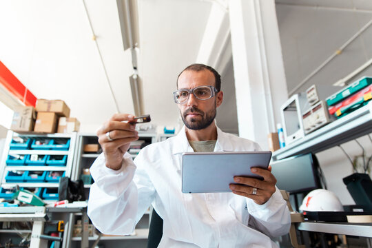 Lab technician analyzing microchip with tablet in electronics workshop