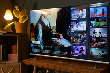 Modern flat screen television displaying streaming service interface with various movie and series thumbnails, showing close up of businesswoman holding clipboard in crime documentary preview