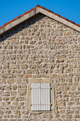 exterior details of old stone wall and tiled roof of building as background and white wooden blinds