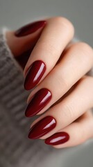 Close-up of female hand with deep red manicure on gray background