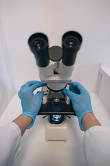 Gloved hands positioning a microscope slide on a microscope stage, ready for scientific observation
