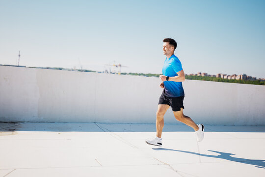 Man jogging on a rooftop in a blue shirt during daytime in the city - Powered by Adobe