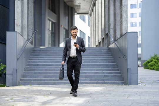 Businessman walking down urban stairs using smartphone and carrying a briefcase, representing concepts of modern communication, business travel, and technology integration
