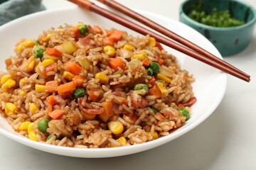 Tasty fried rice and chopsticks on white table, closeup