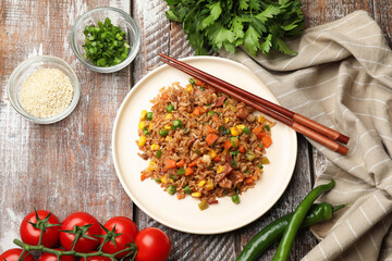 Delicious fried rice with vegetables and bacon served on wooden table, flat lay