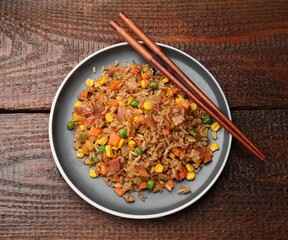Delicious fried rice with vegetables and chopsticks on wooden table, top view