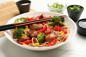 Delicious noodles with meat and vegetables served on white marble table, closeup