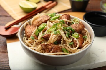 Tasty noodles with chicken, green peppers and sesame seeds served on wooden table, closeup
