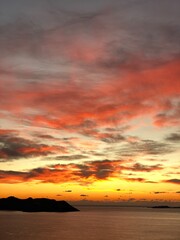 Fototapeta premium Vibrant sunset sky over ocean with dramatic clouds and silhouettes, ideal for background