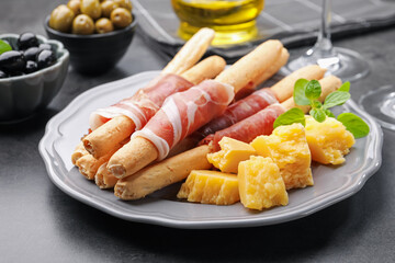 Grissini breadsticks with prosciutto, cheese and olives on grey table, closeup