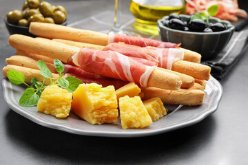 Grissini breadsticks with prosciutto and cheese on grey table, closeup